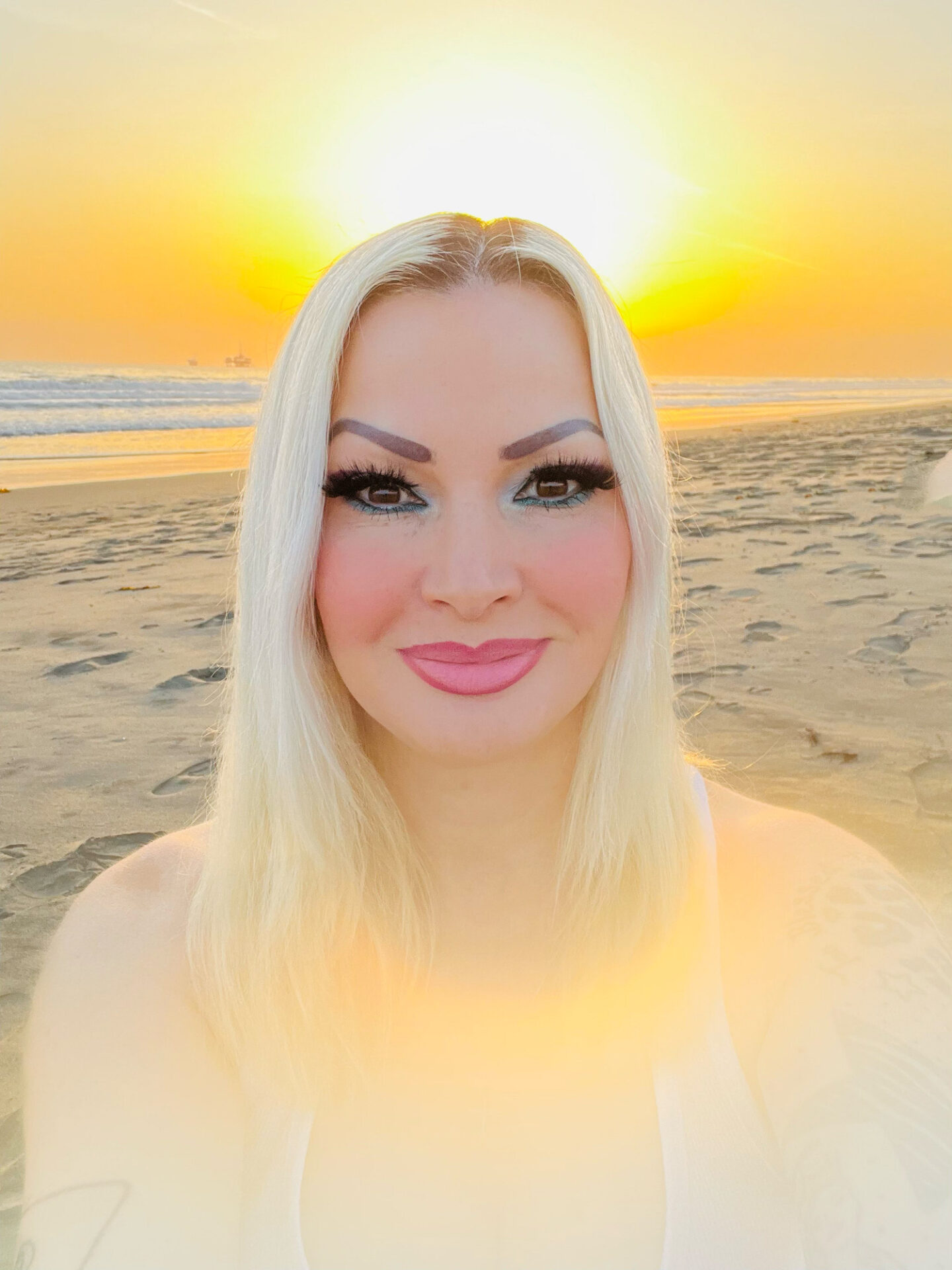 A woman with white hair and pink lipstick on the beach.