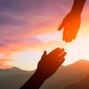 Two hands reaching out towards each other in the sunset.